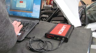 A J2534 pass-thru device, such as the Launch Tech J-Box, connects the vehicle by way of the OBD-II port, and a laptop computer, to complete vehicle reprogramming.