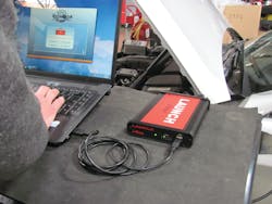 A J2534 pass-thru device, such as the Launch Tech J-Box, connects the vehicle by way of the OBD-II port, and a laptop computer, to complete vehicle reprogramming.