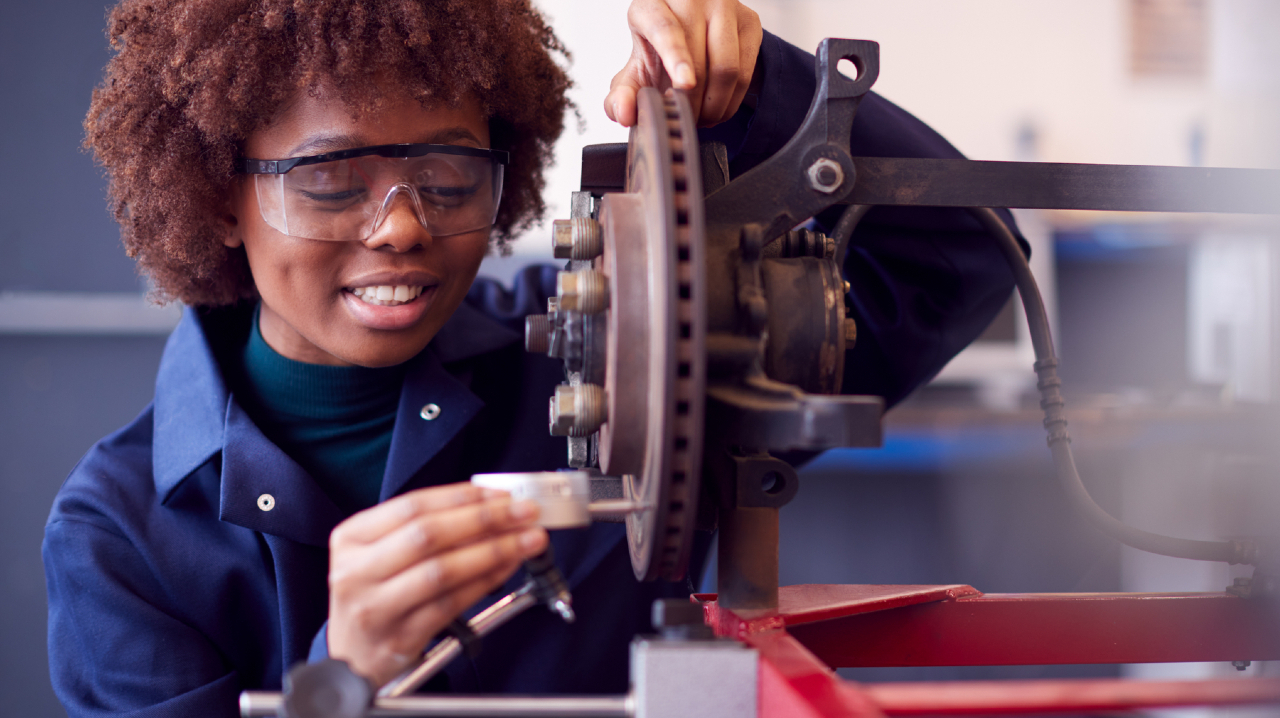 Female student working on car brakes on auto mechanic apprenticeship course at college
