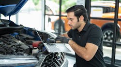 Technician with laptop under hood of car