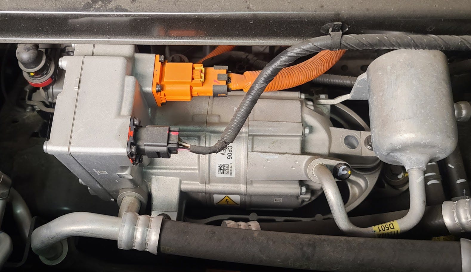 This is a close-up of the electric A/C compressor assembly on the 2023 Hyundai IONIQ 6 RWD, you can see that the compressor has the rear mounted PIM with the DC high-voltage connector in orange and the low-voltage control wiring in black