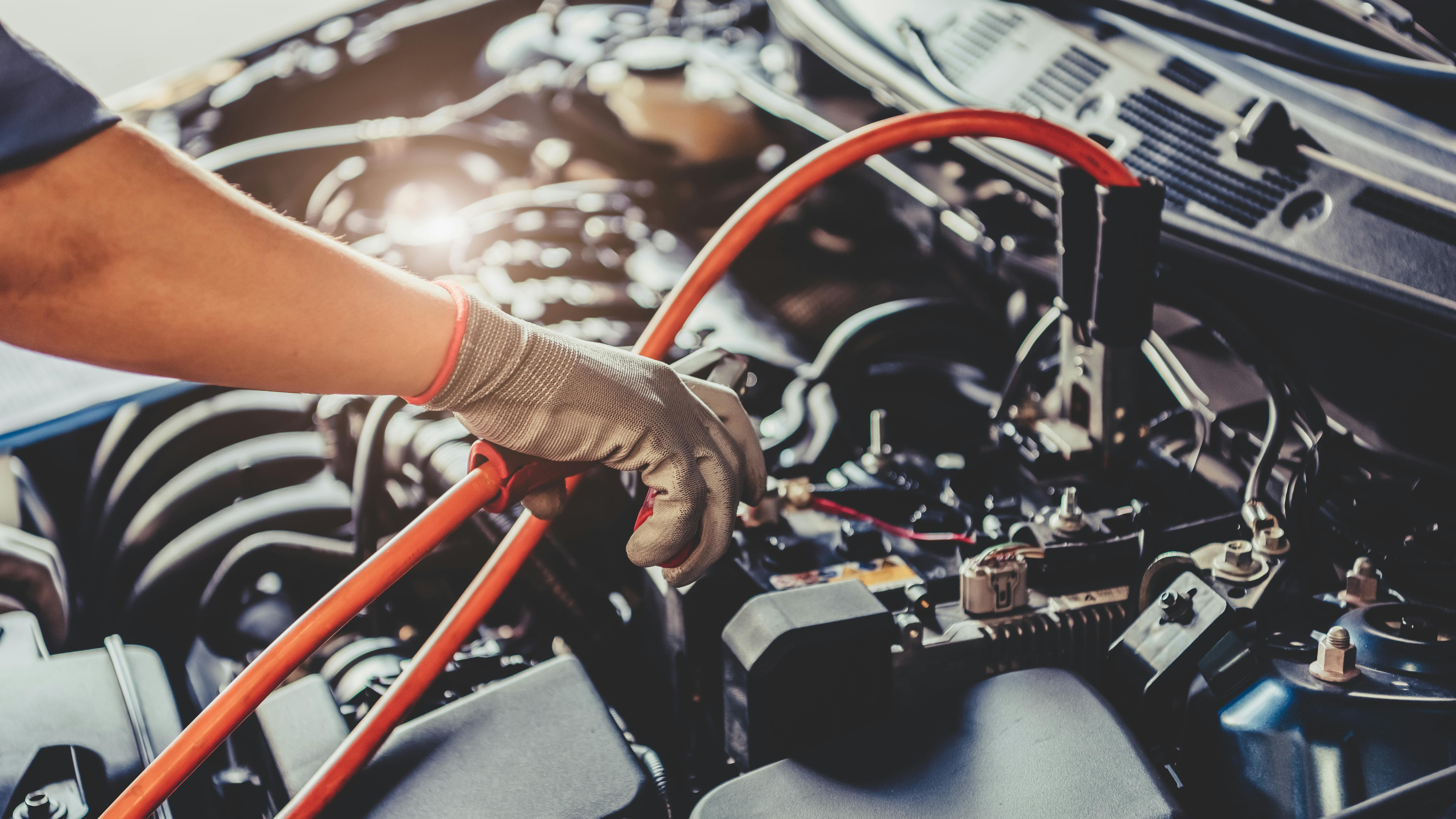 a person puts jumper cables on a car battery