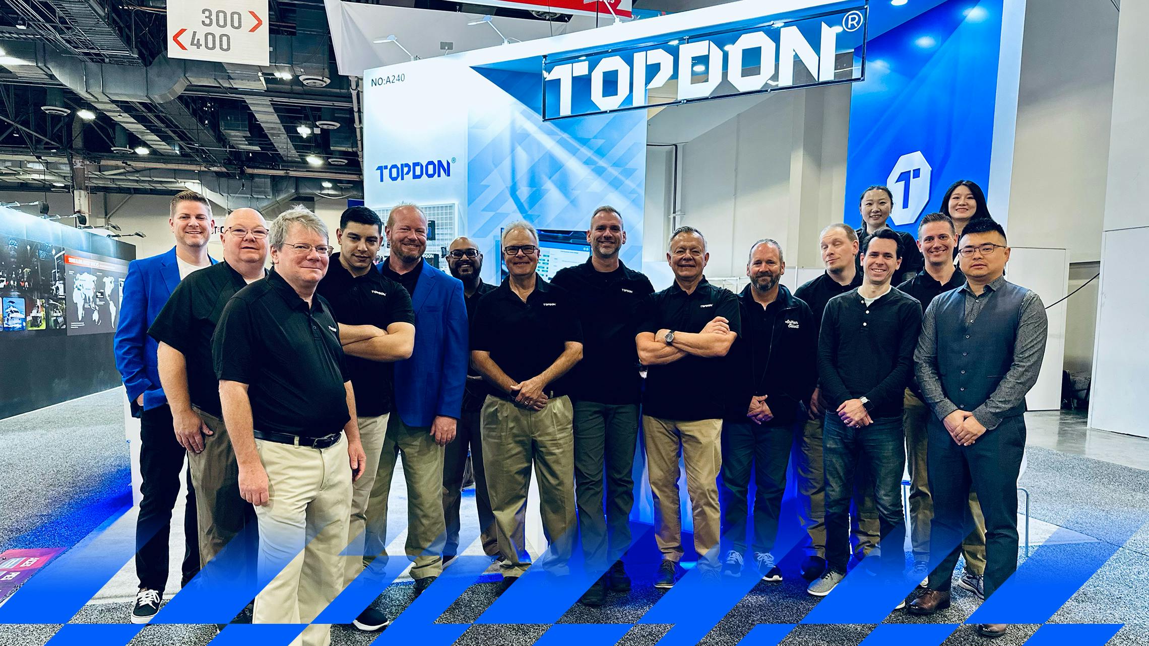 16 TOPDON employees in similar TOPDON-branded outfits smile together in front of a TOPDON booth at a convention