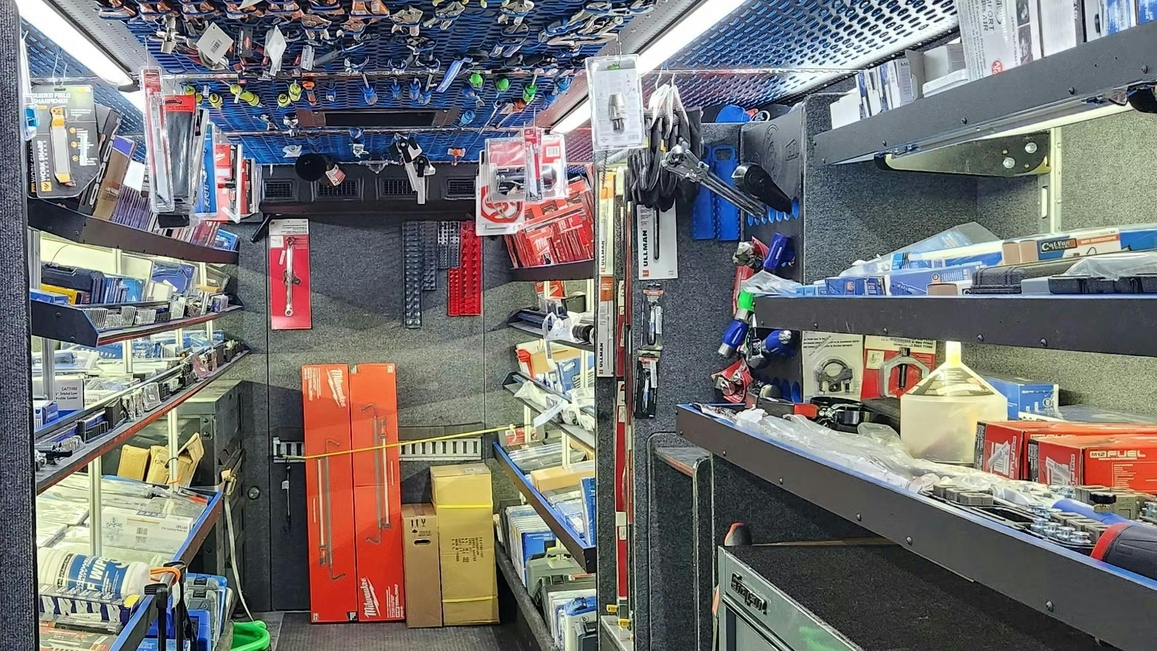 the interior of a tool truck with gray carpeting on the walls with grey metal shelves full of tools and boxes on either side of the truck