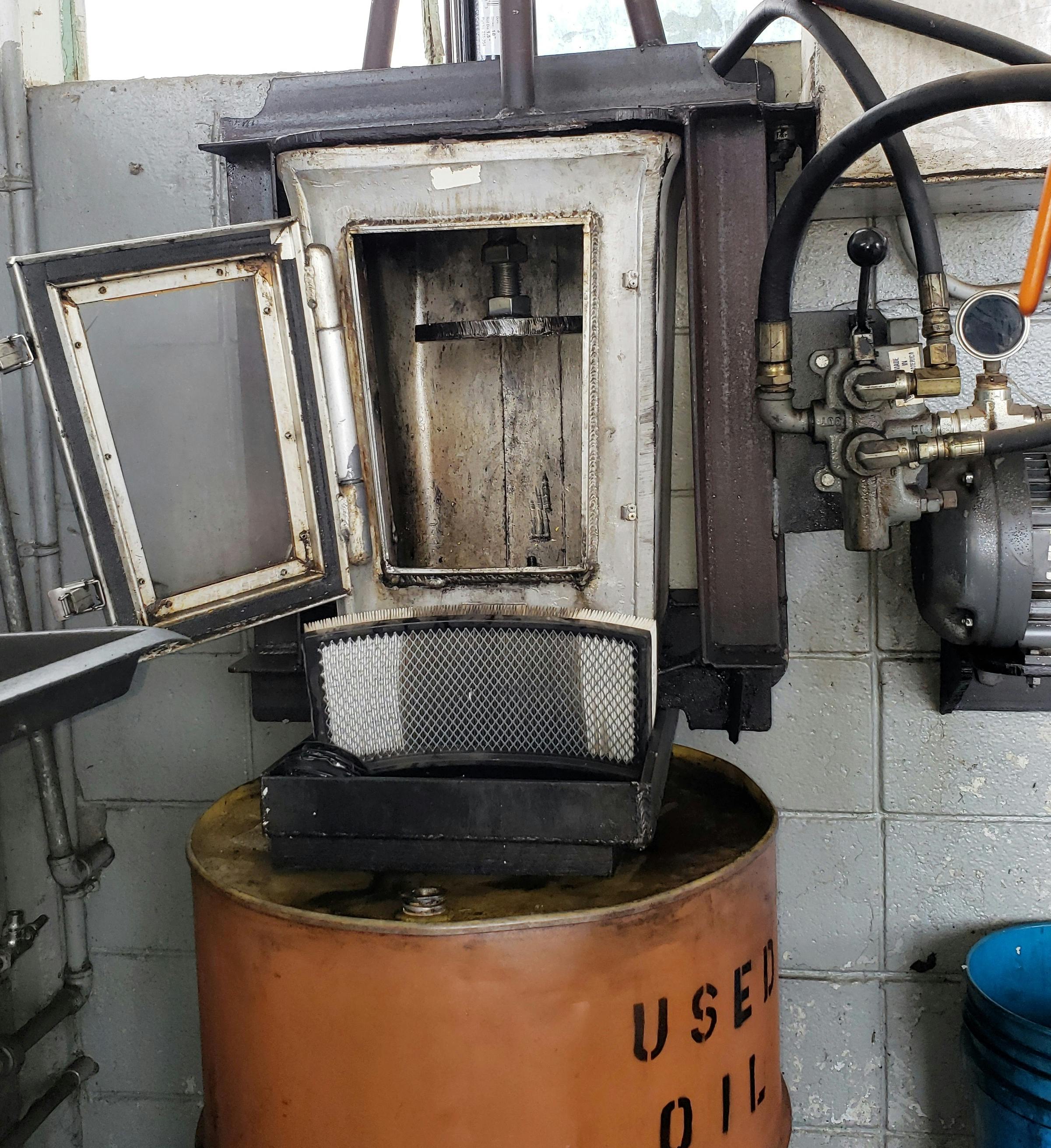 Example of an oil filter crusher. The used engine oil filter is placed in the unit and a hydraulic ram extends downward and crushes the filter. In this example, the oil that is squeezed out runs through an air filter before being drained into the used oil barrel.
