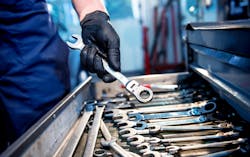 a person in mechanic's coveralls holds a ratcheting wrench above an open tool drawer of wrenches a person in mechanic's coveralls holds a ratcheting wrench above an open tool drawer of wrenches