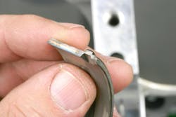 Note the small tang on this main bearing. All main and rod bearings will feature a locating tang. This is designed to simply position the bearing in its saddle during assembly. Locating tangs do not prevent bearing shell rotation. Bearings “lock” in place as a result of bearing crush when the upper and lower shells mate during cap installation. Note the small tang on this main bearing. All main and rod bearings will feature a locating tang. This is designed to simply position the bearing in its saddle during assembly. Locating tangs do not prevent bearing shell rotation. Bearings “lock” in place as a result of bearing crush when the upper and lower shells mate during cap installation.